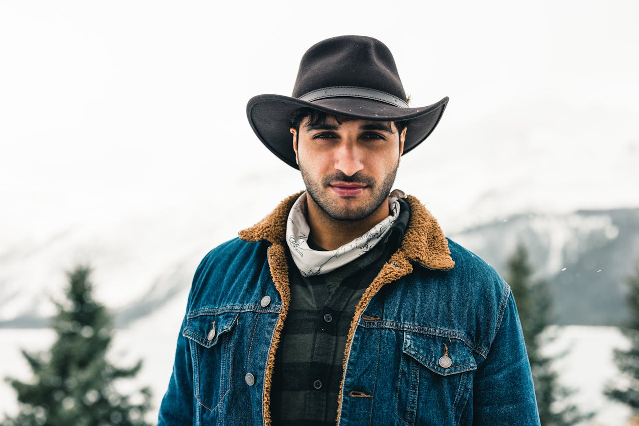 about-us-01 Man in denim jacket and cowboy hat stands outdoors in snowy Jasper, Canada.