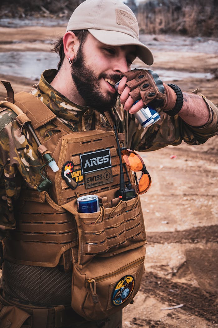 services-01 A man in tactical gear enjoys an energy drink in an outdoor setting, showcasing adventure and readiness.